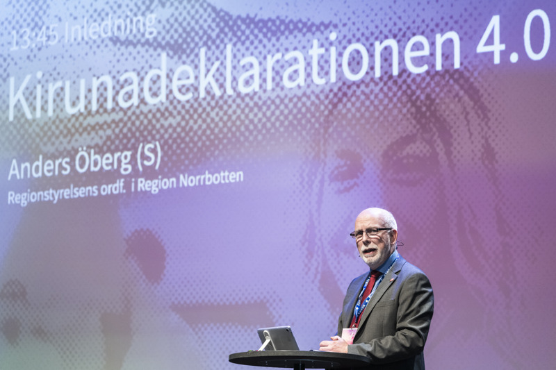 En person står vid ett bord framför en storbildskärm. 