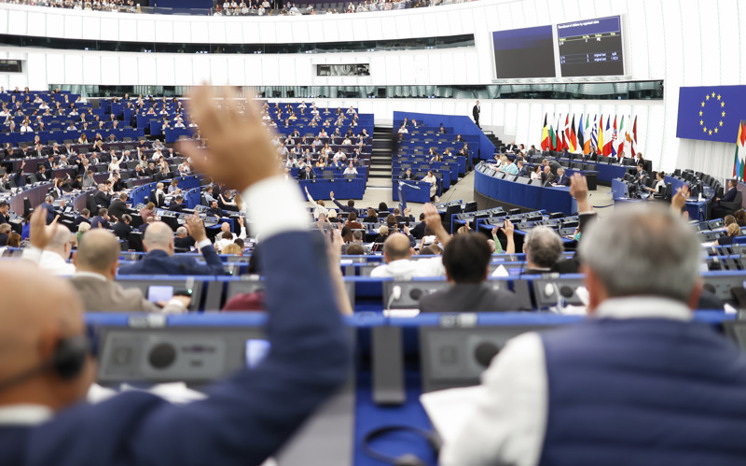 En grupp personer deltar i votering i en mötessal hos Europaparlamentet.