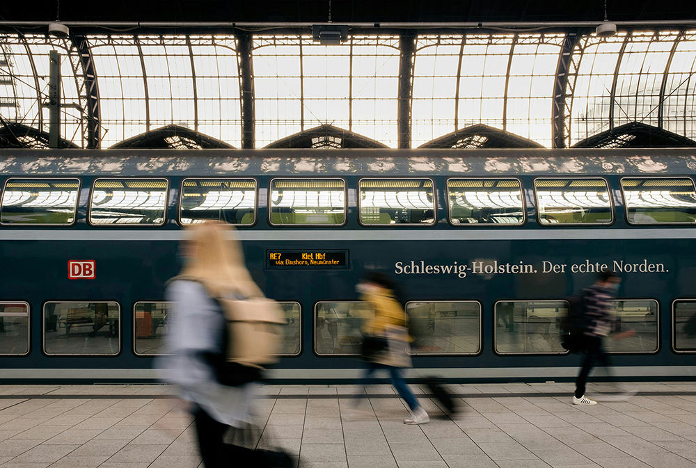 Train at a station in Hamburg, passengers passing by with bags.